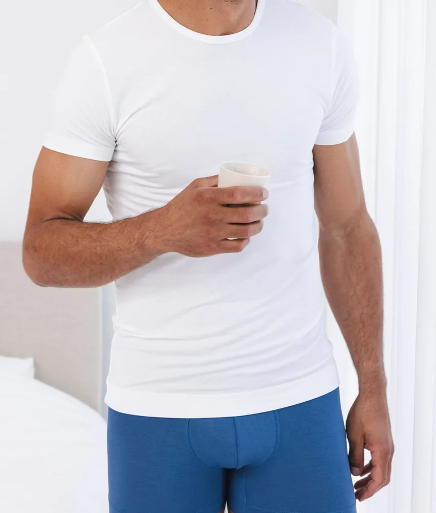 Man in een wit Undiemeister ondershirt en blauwe boxershort, met een kop koffie